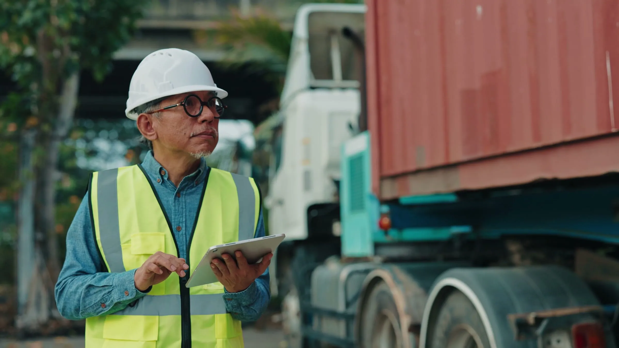 A fleet engineer in a hard hat and safety vest checks a tablet next to a truck.