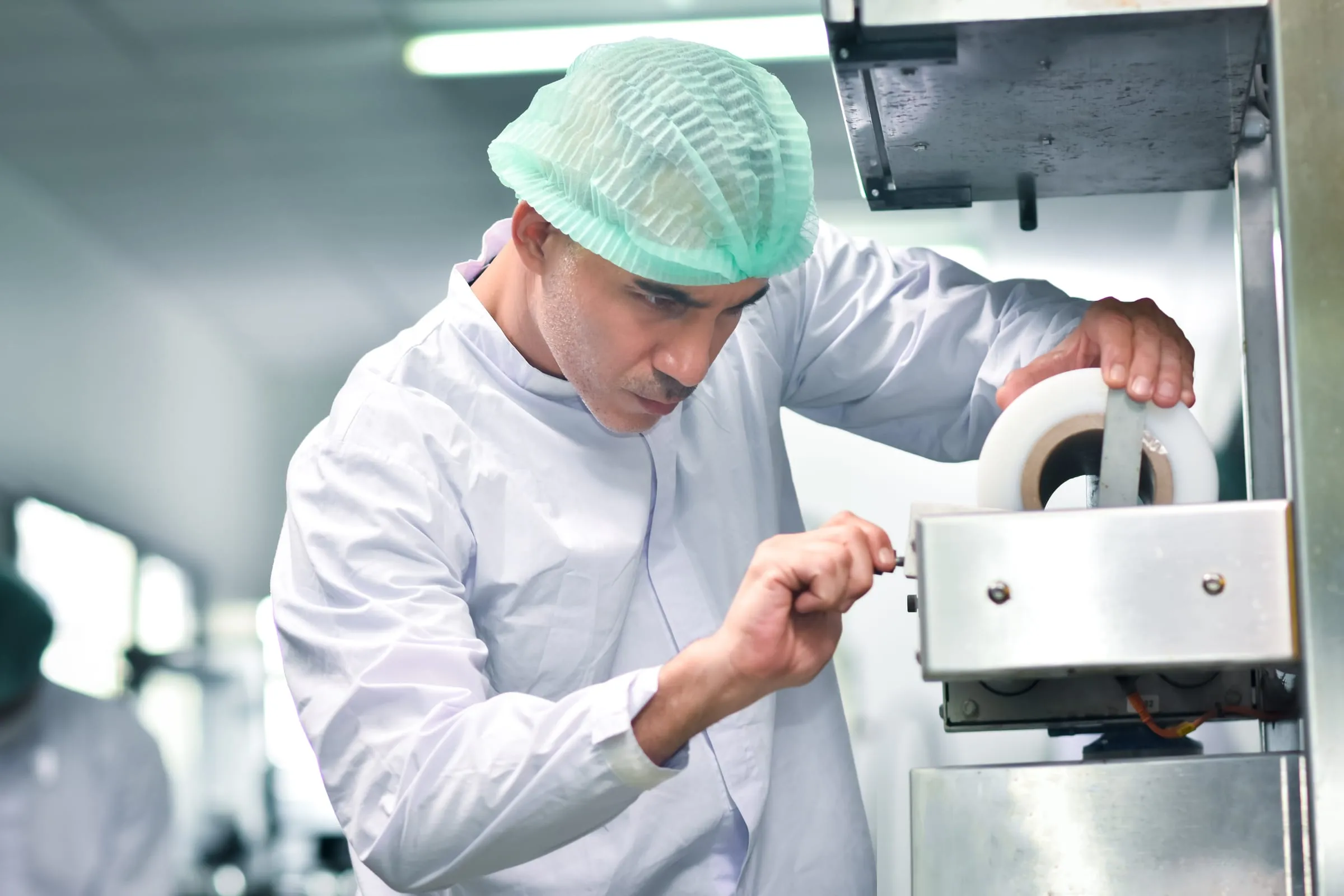 A technician in a hairnet adjusts a machine on a food production line.